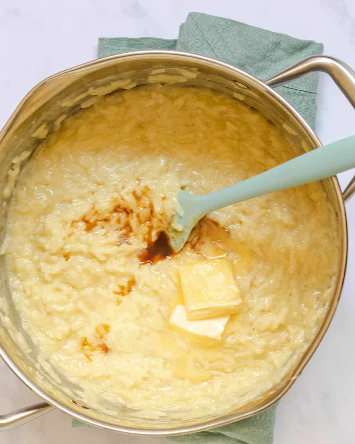 butter and vanilla extract added to pot of rice pudding with a rubber spatula 