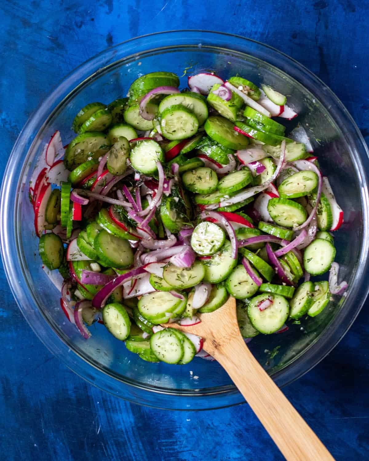 cucumber radish salad with dressing in a glass bowl with mixing spoon