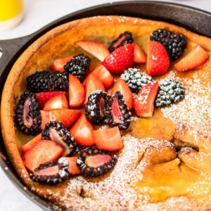 gluten free dutch baby in cast iron skillet with strawberries and blackberries