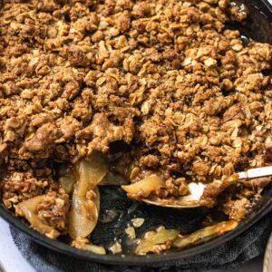 gluten free bourbon apple crisp in cast iron skillet with serving spoon