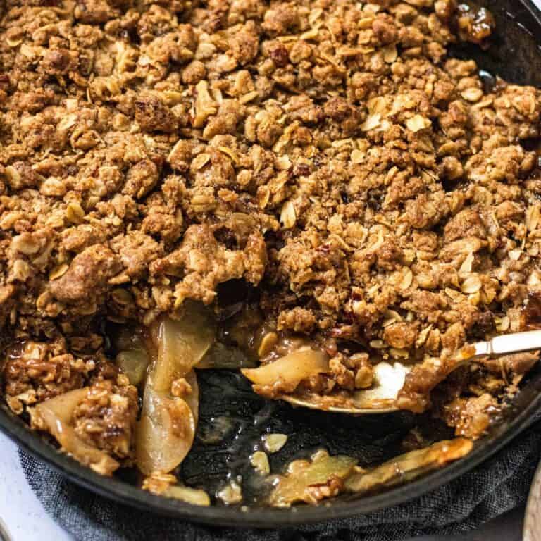 gluten free bourbon apple crisp in cast iron skillet with serving spoon