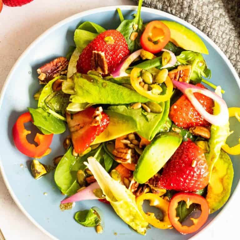 strawberry spinach salad on a blue plate with pecans and avocado