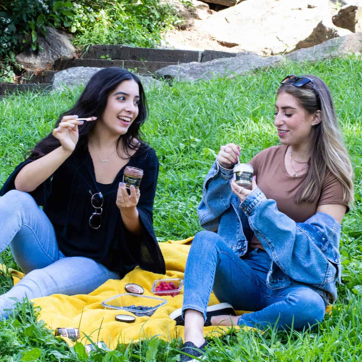 two friends enjoying zen pudding at the park on a yellow blanket