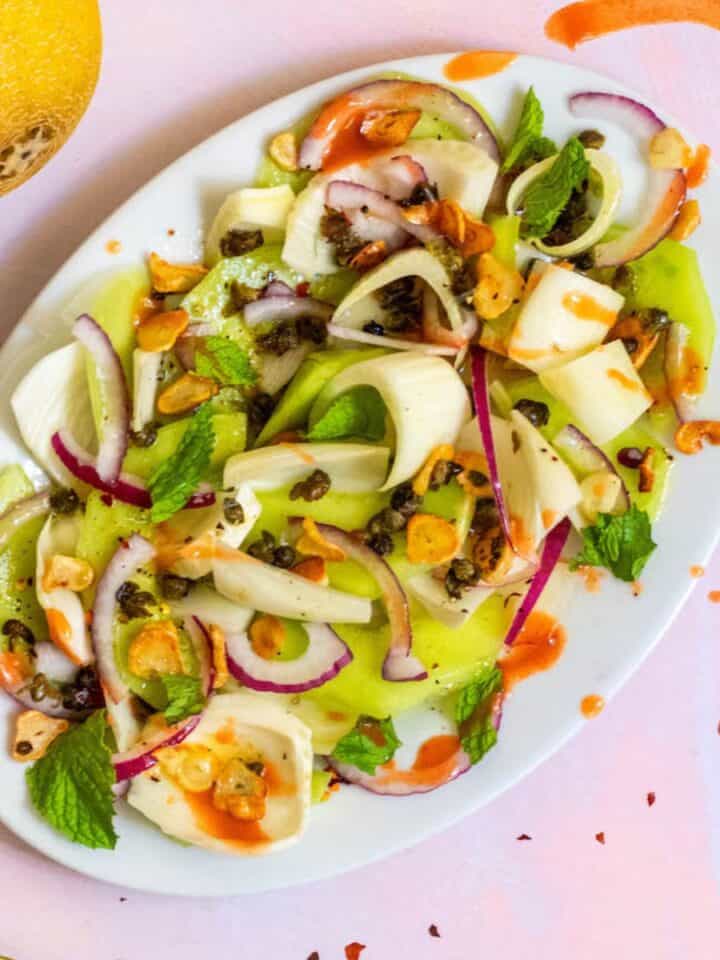Summer Fennel Salad with Melon on a white dish with hot sauce and pink background