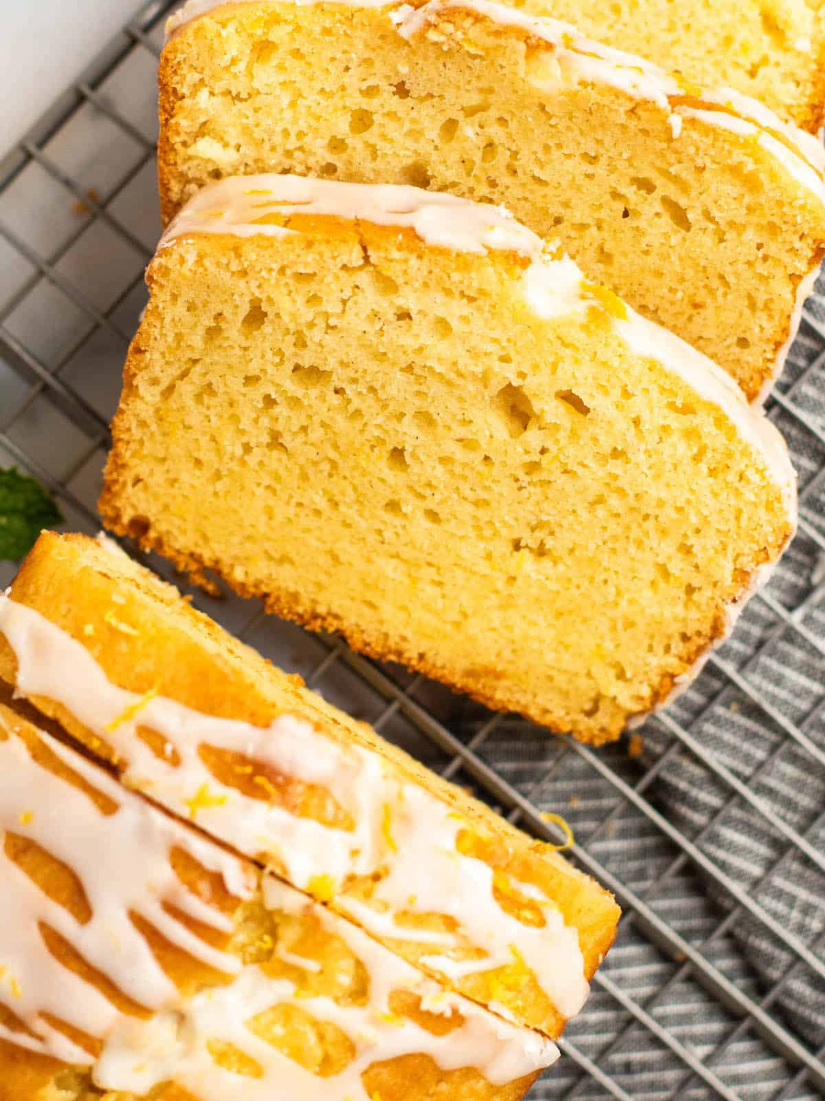 sliced gluten free lemon drizzle cake on a wire baking rack with towel underneath