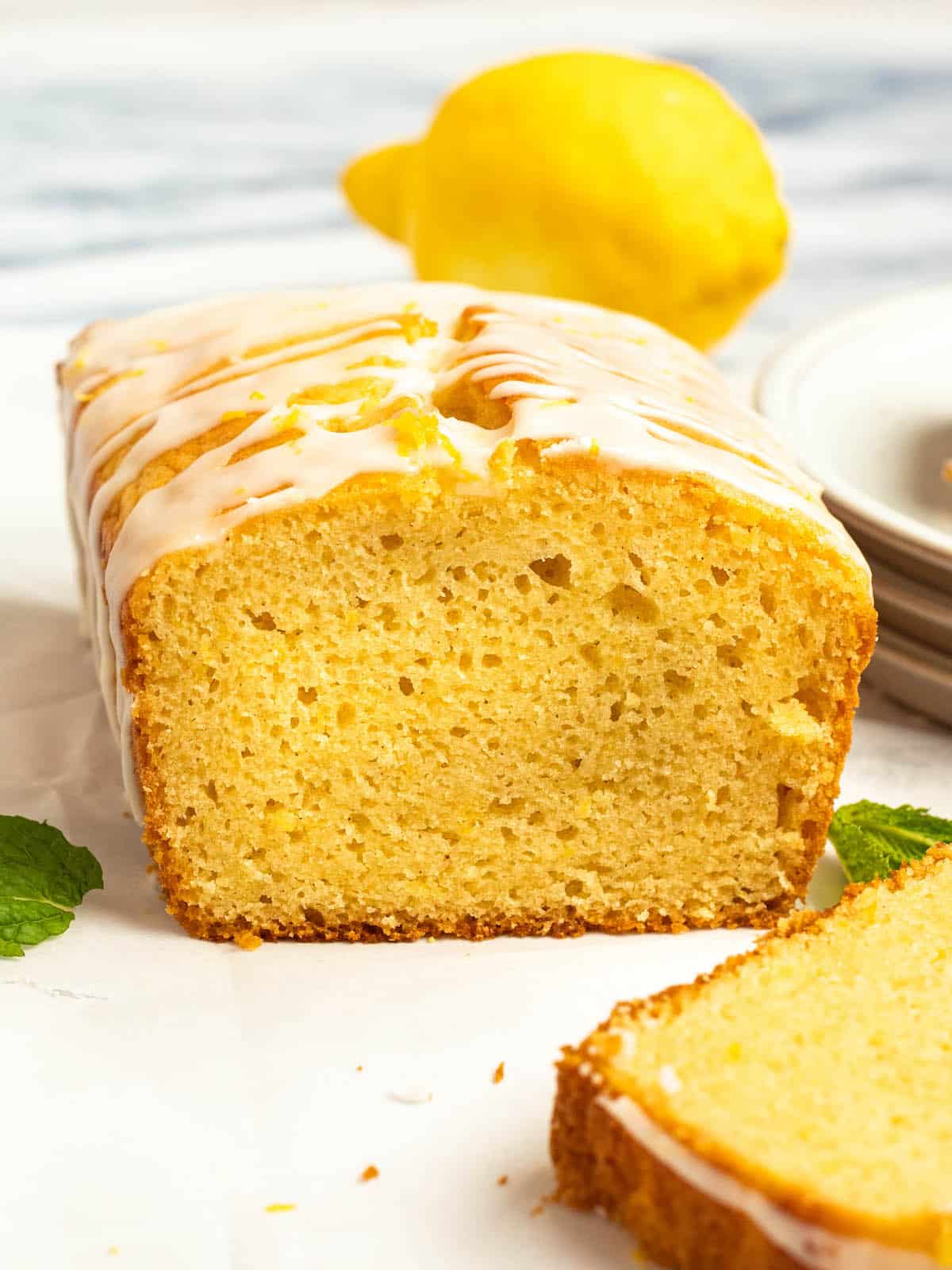 sliced open gluten free lemon drizzle cake on a white counter with lemon in background