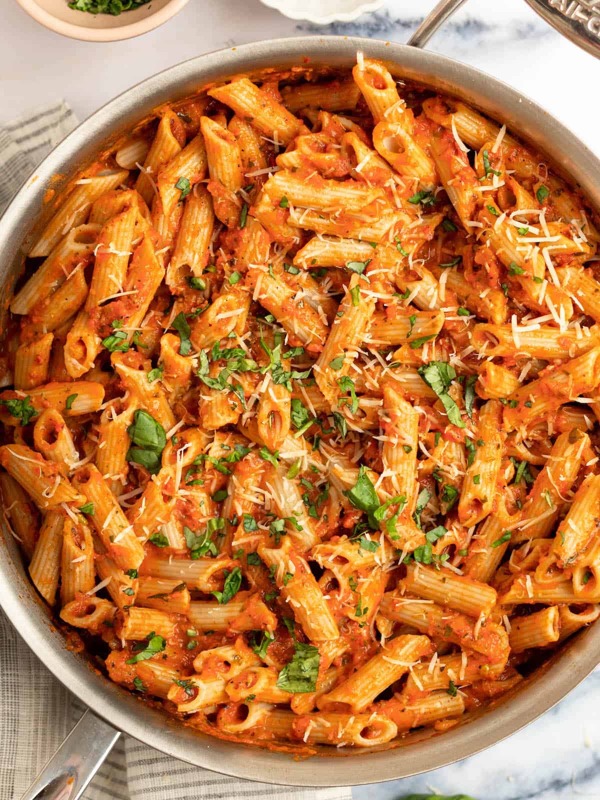 pink pasta in an all clad pan with a dish towel on the side