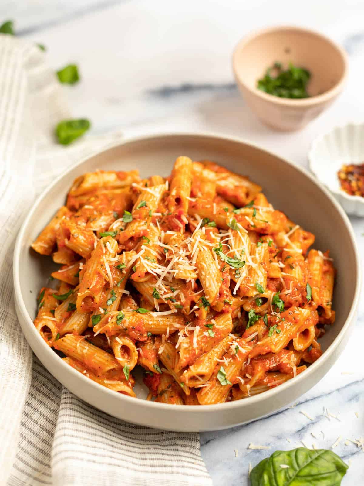 pink pasta in a wide bowl with basil garnishes and dish towel on the side