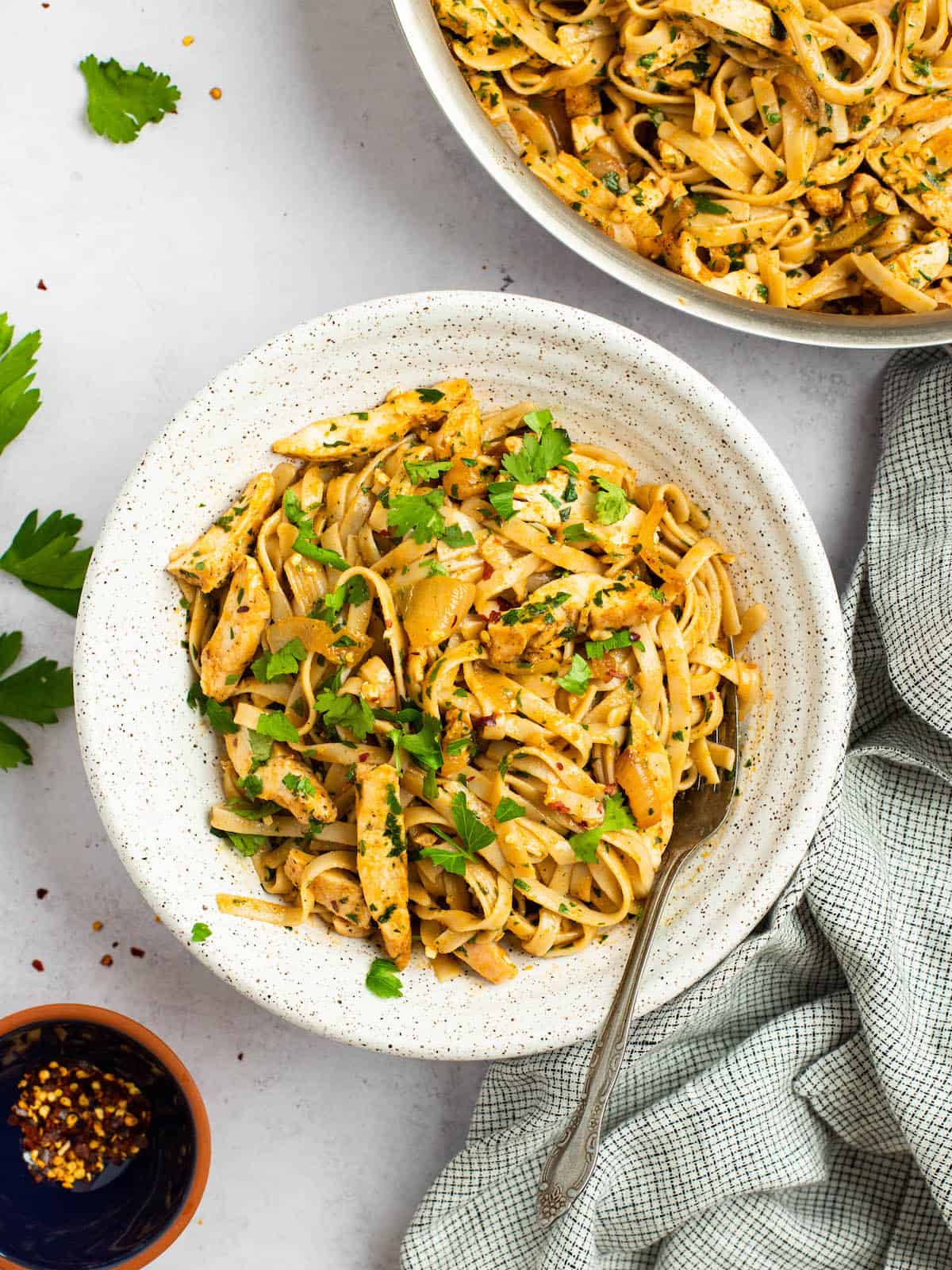 spicy chicken pasta in a ceramic bowl with a fork and skillet with pasta in the background 