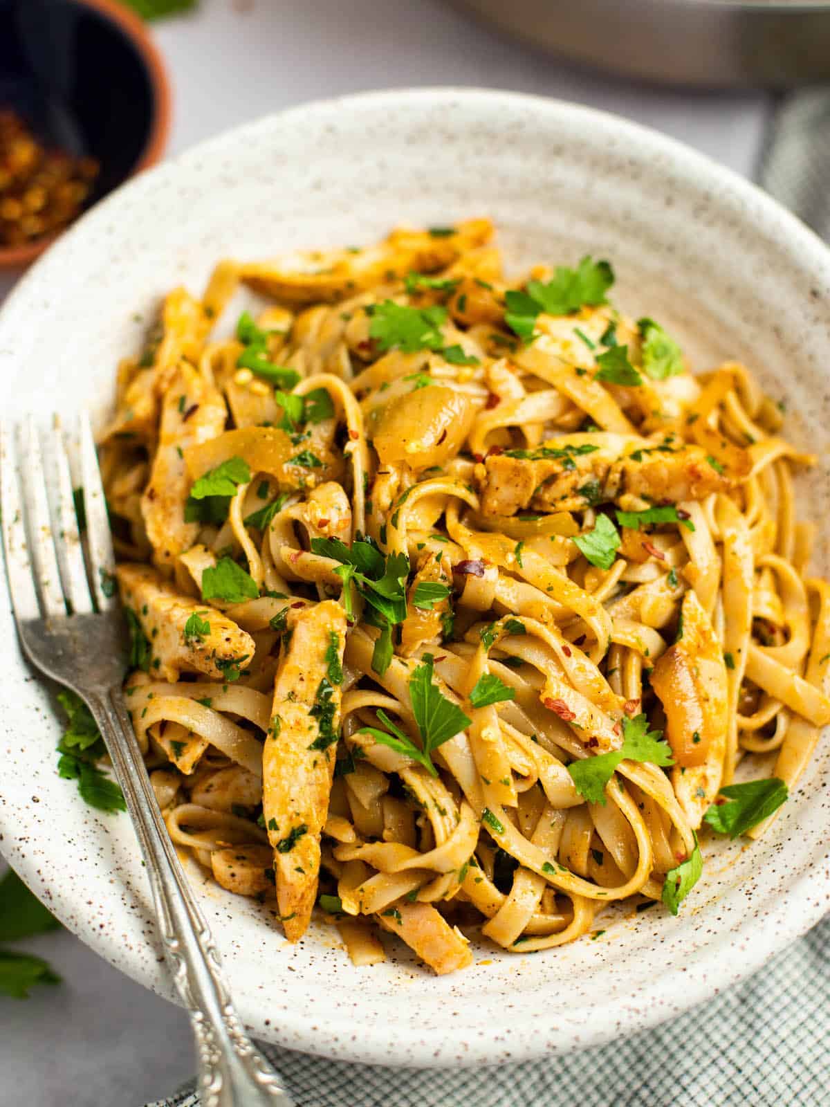 spicy chicken pasta in a ceramic bowl with a fork and cilantro and parsley garnish