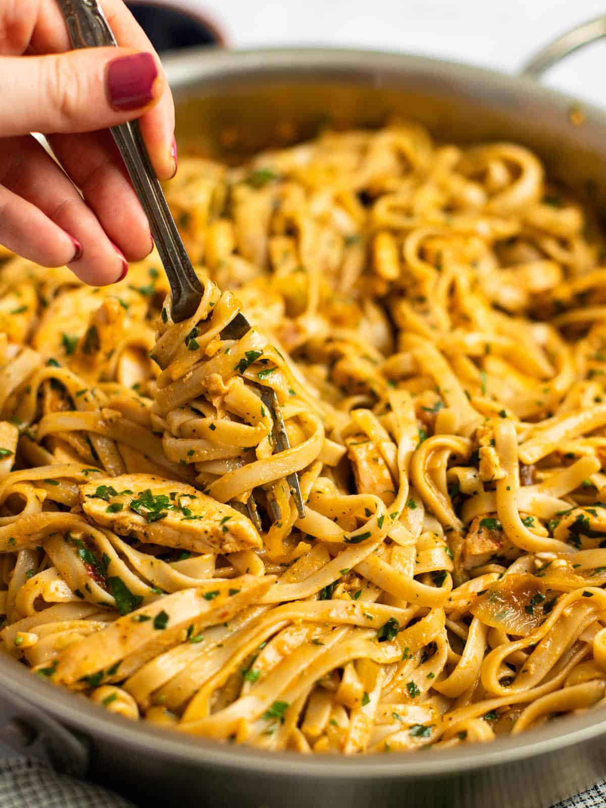 spicy chicken pasta twirled on a fork in a large skillet