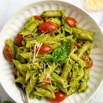tuna pesto pasta with cherry tomatoes in a white bowl with parmesan