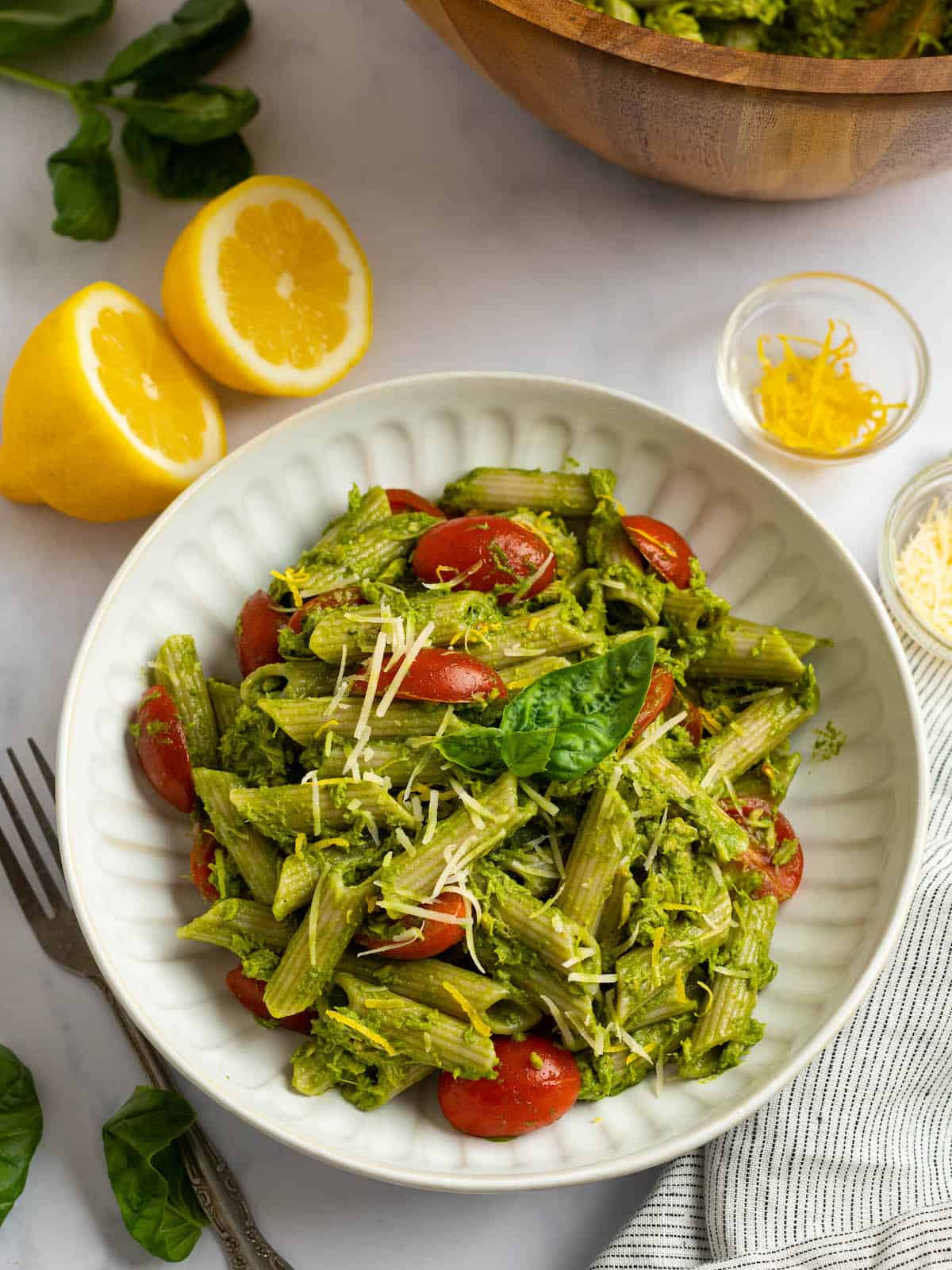 tuna pesto pasta in a white bowl with towel on the side and lemon in background