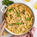 penne alla salmone in a white dutch oven with basil and serving spoons