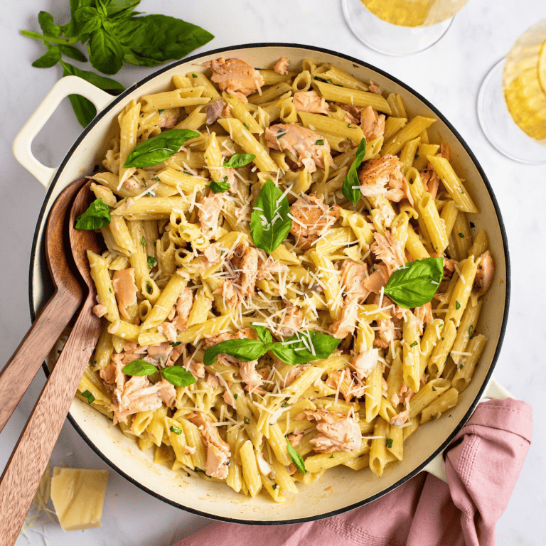 penne alla salmone in a white dutch oven with basil and serving spoons
