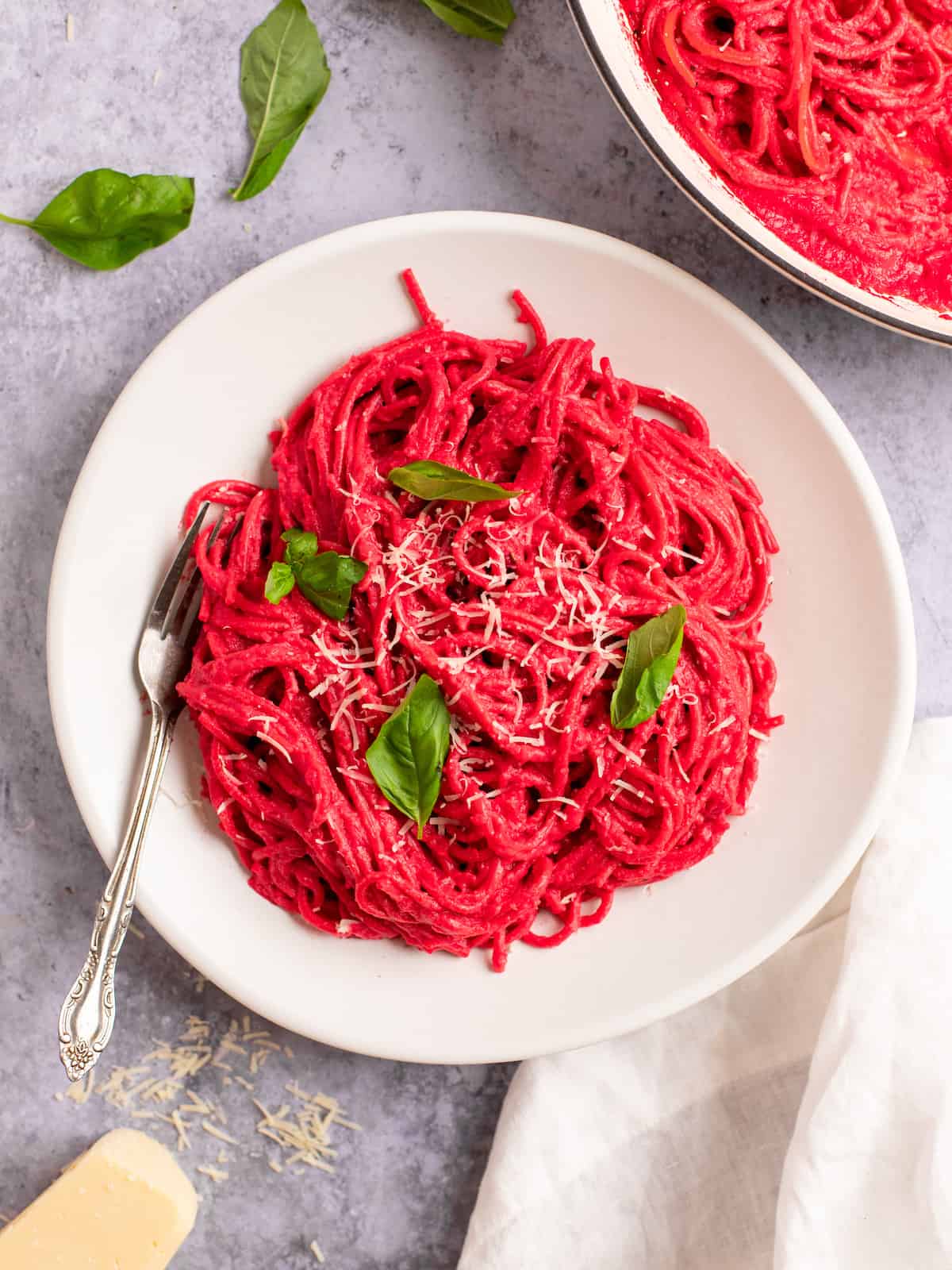 pink barbie pasta on a white plate with a fork and parmesan and basil