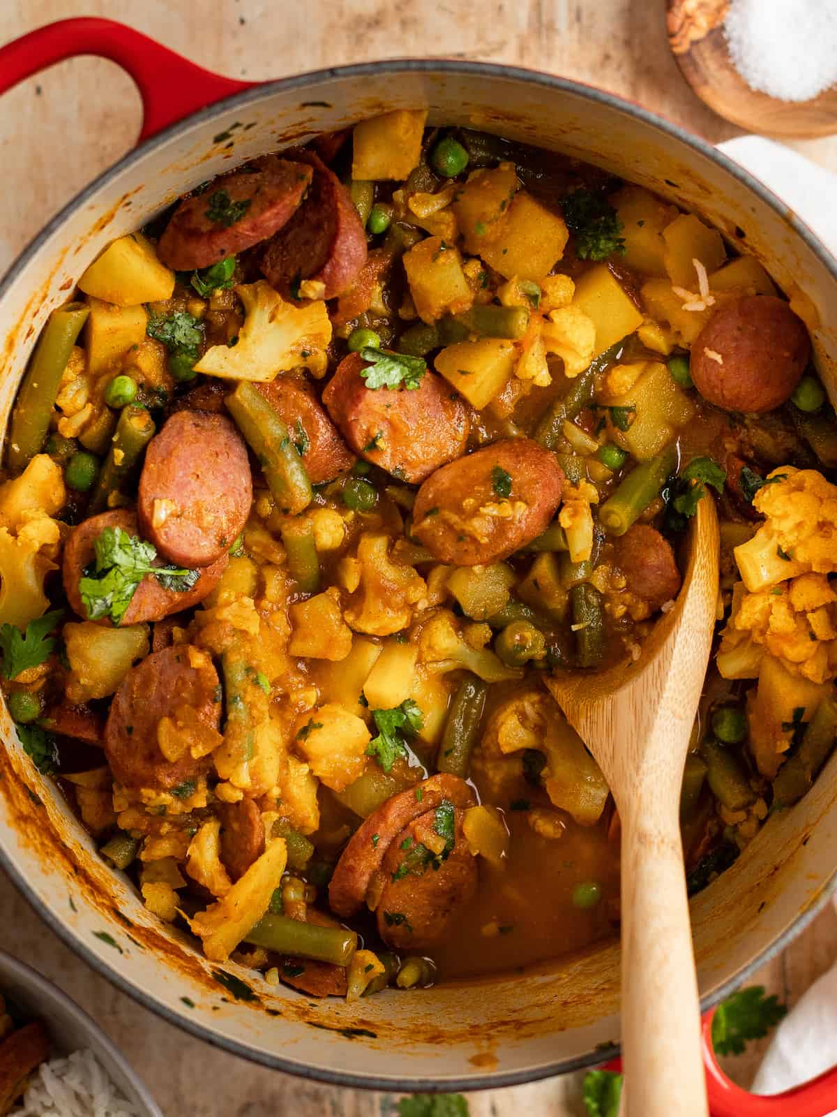 sausage curry in a dutch oven with a wooden spoon