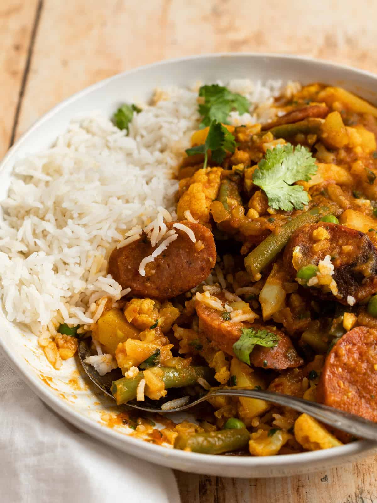 sausage curry in a bowl with basmati rice and a spoon