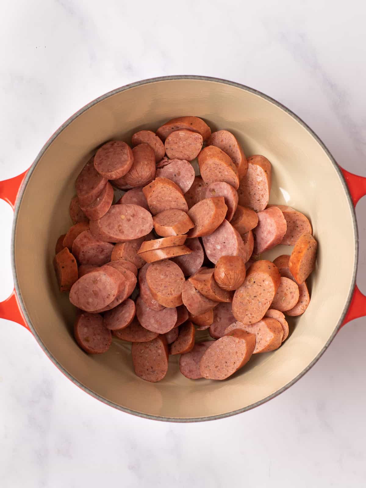 raw sausages added to a red dutch oven 