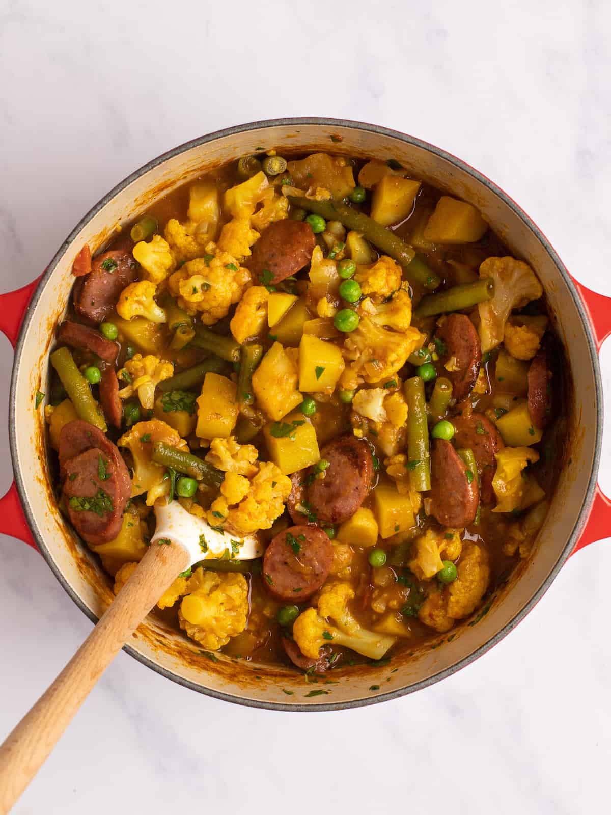 pot of sausage curry with a wooden spatula 