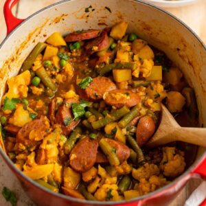 sausage curry in a dutch oven with a wooden spoon