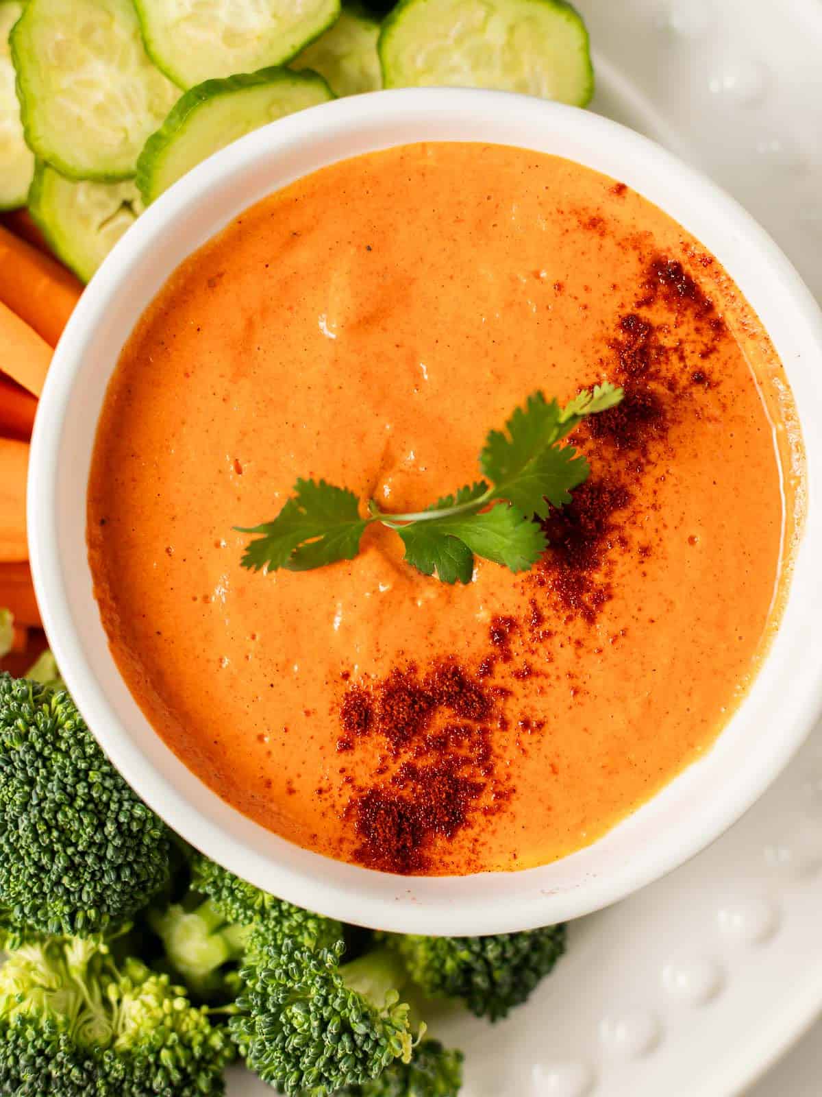 smokey red pepper crema in a white bowl with broccoli and cucumbers