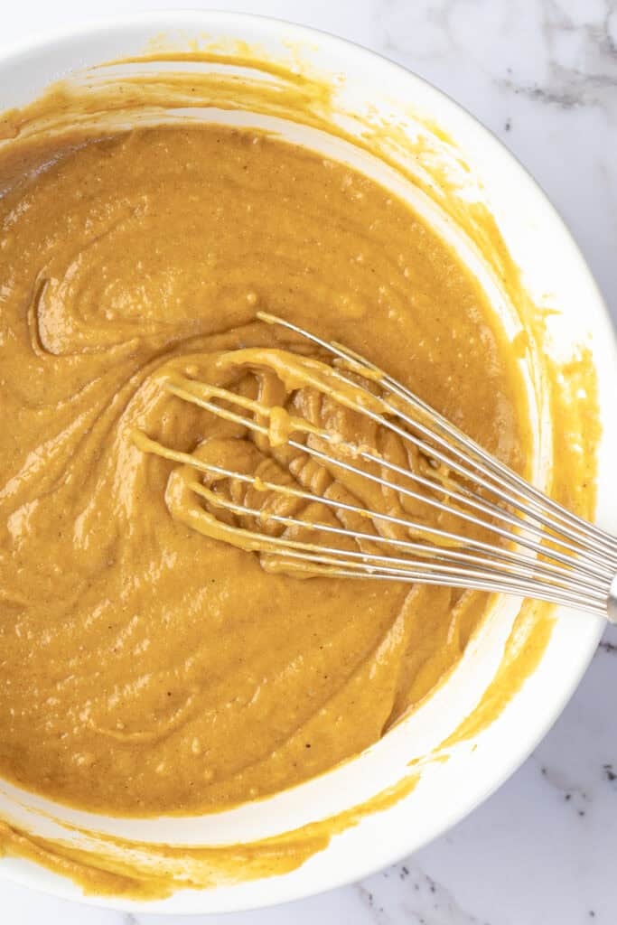 gluten free pumpkin cake batter in a white bowl with a whisk