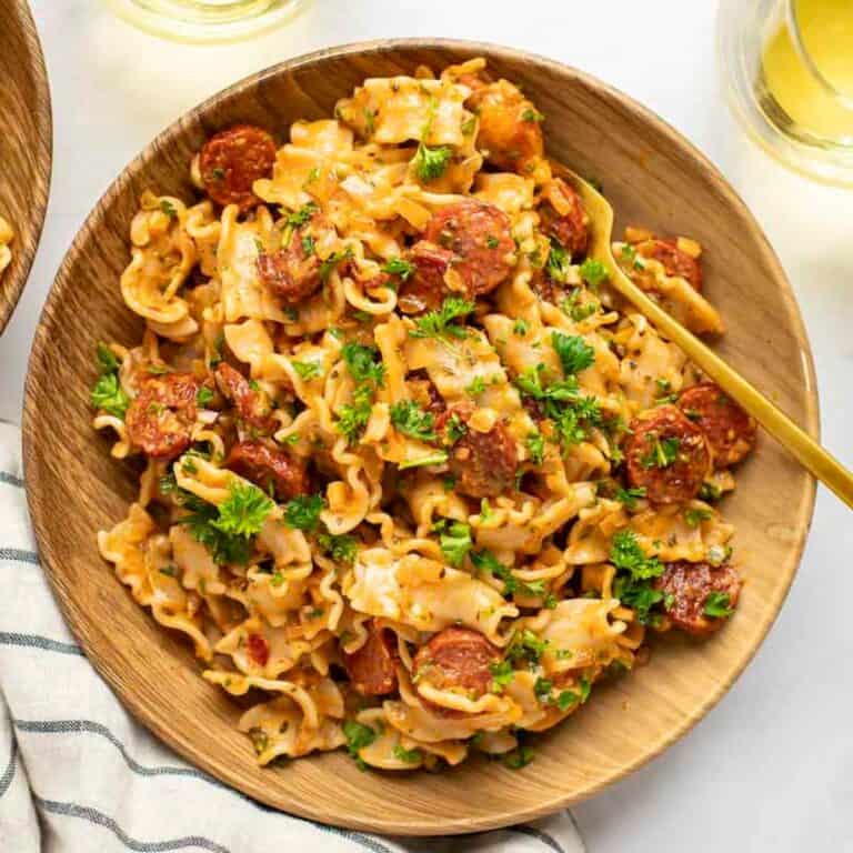 spicy sausage pasta in a wooden bowl with gold fork and white wine