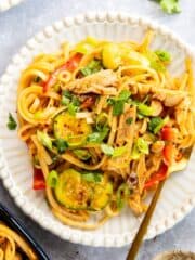 Spicy Sesame Chicken Rice Noodles on a white plate with gold fork