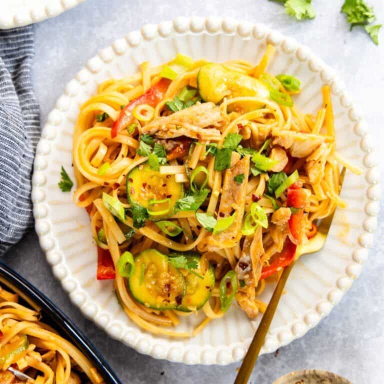 Spicy Sesame Chicken Rice Noodles on a white plate with gold fork