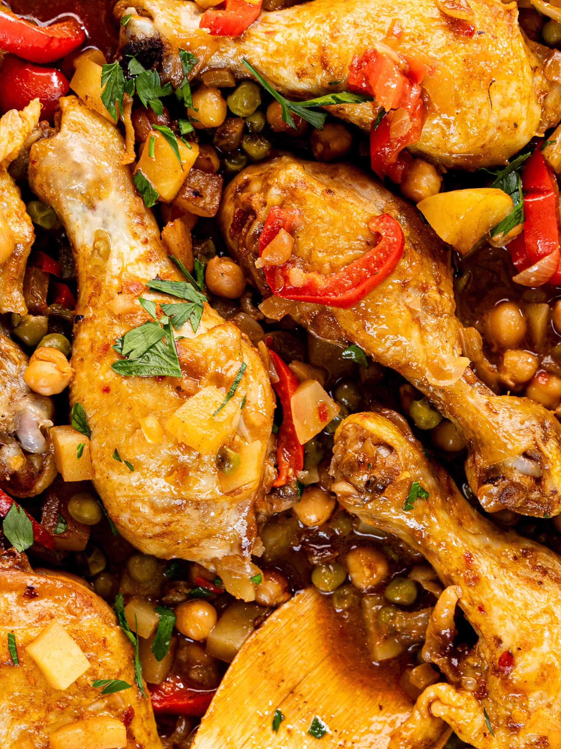 close up of three braised chicken drumsticks with red pepper and chickpeas
