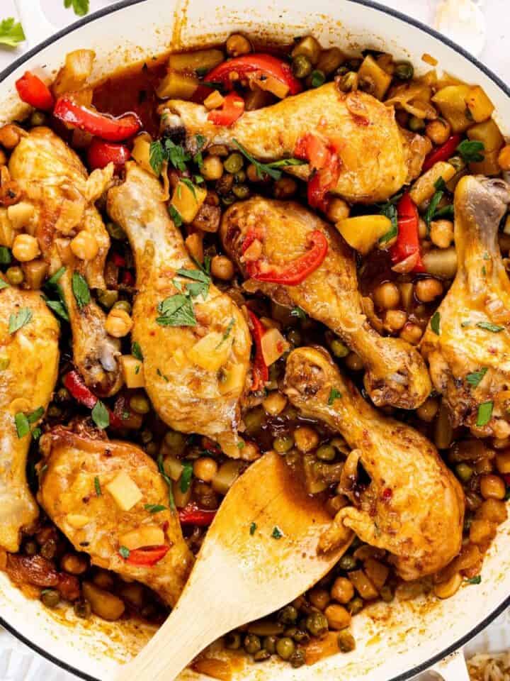 Braised Chicken Drumsticks with Potatoes and Chickpeas in a white skillet with a wooden spoon