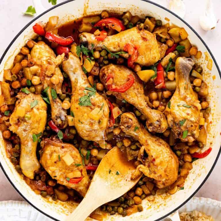 Braised Chicken Drumsticks with Potatoes and Chickpeas in a white skillet with a wooden spoon