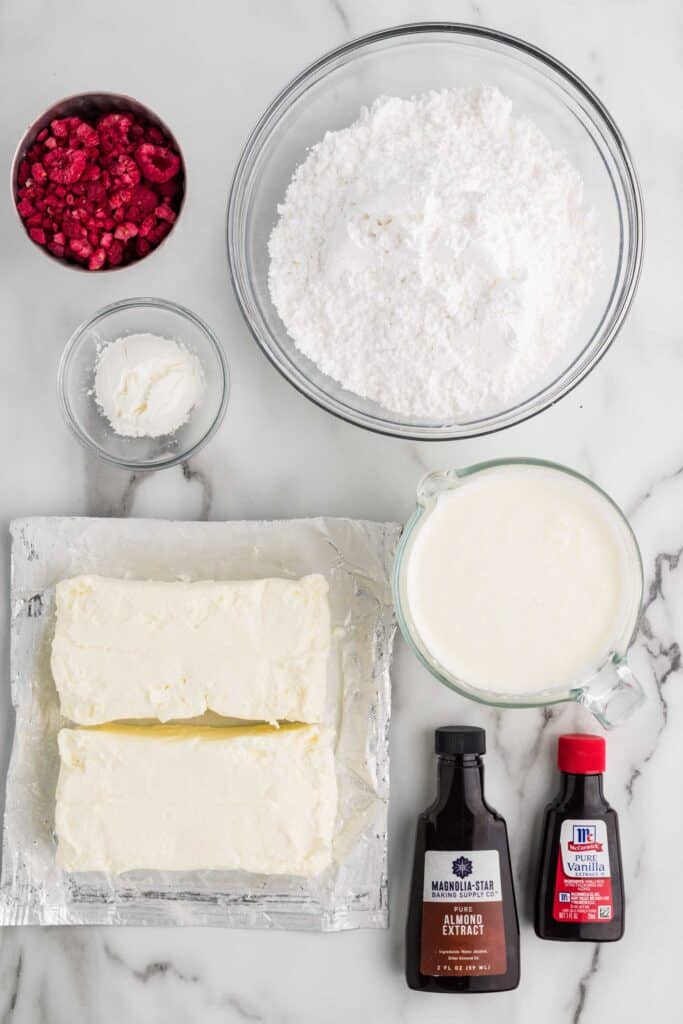 Overhead flat lay of ingredients for raspberry cheesecake filling: cream cheese, powdered sugar, freeze-dried raspberries, heavy cream, almond extract, and vanilla extract