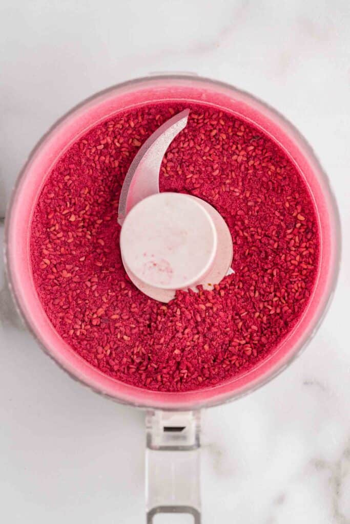 Overhead view of freeze-dried raspberries ground into a fine red powder inside a food processor