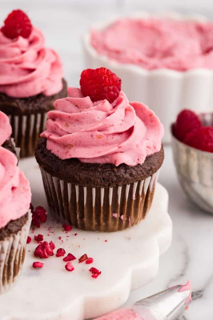Close-up of chocolate cupcakes topped with swirled pink raspberry cheesecake frosting and a fresh raspberry