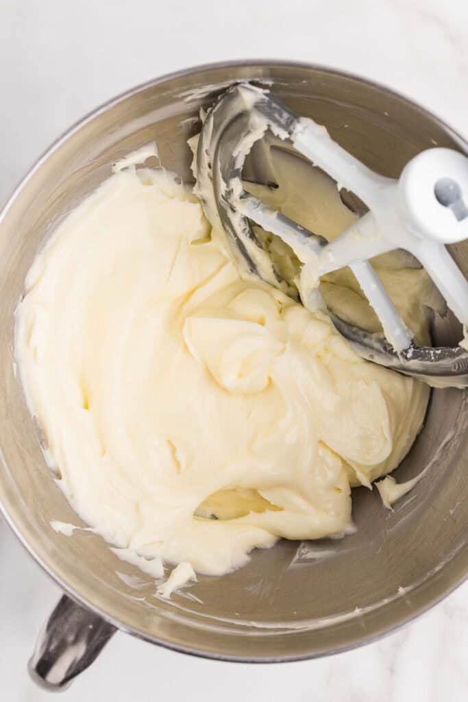 Overhead view of cream cheese beaten until smooth and fluffy in a stand mixer bowl with a paddle attachment
