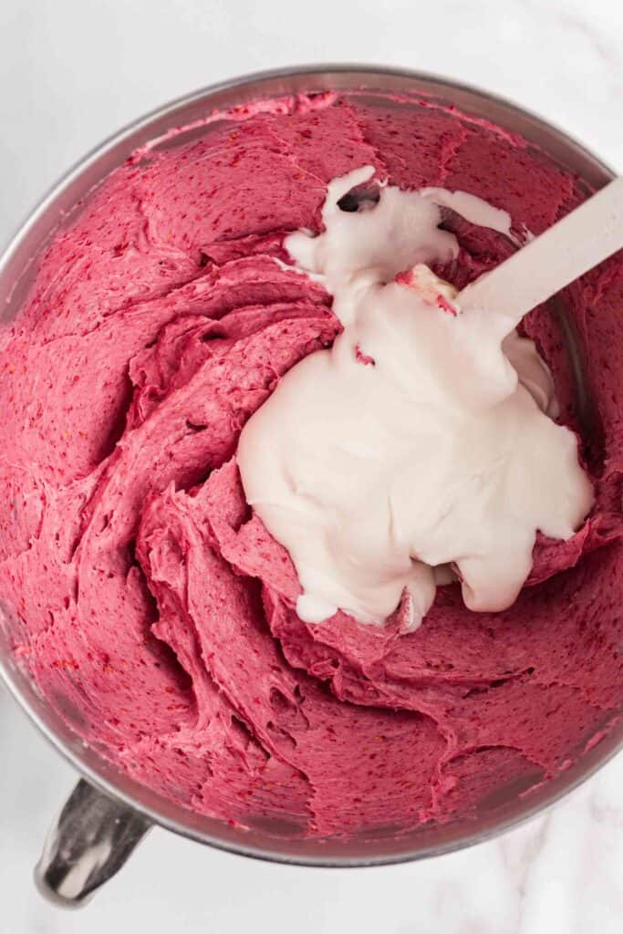 Whipped cream being folded into the pink raspberry cream cheese mixture in a stand mixer bowl