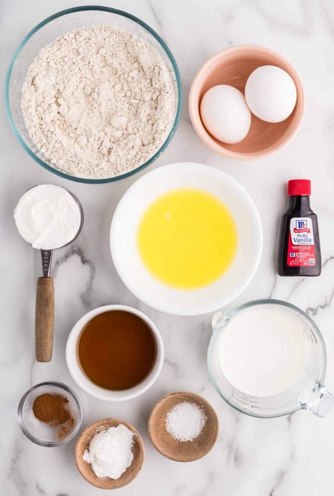 oat flour pancake ingredients flatlay including melted butter, maple syrup, Greek yogurt, milk, vanilla, cinnamon, and salt