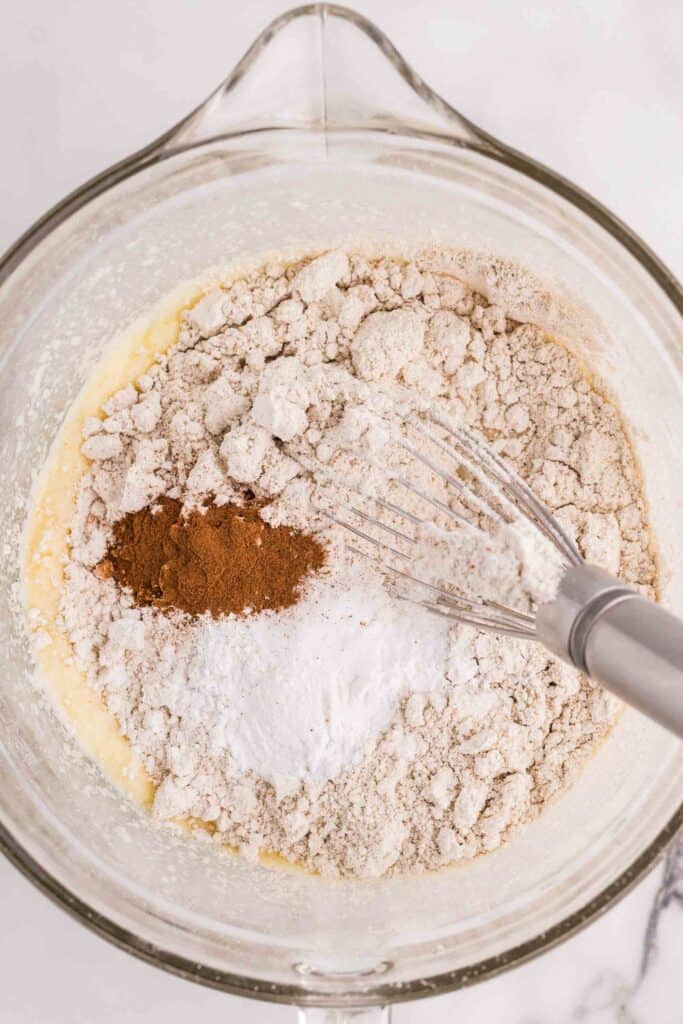 adding oat flour and dry ingredients to the wet batter mixture in a bowl