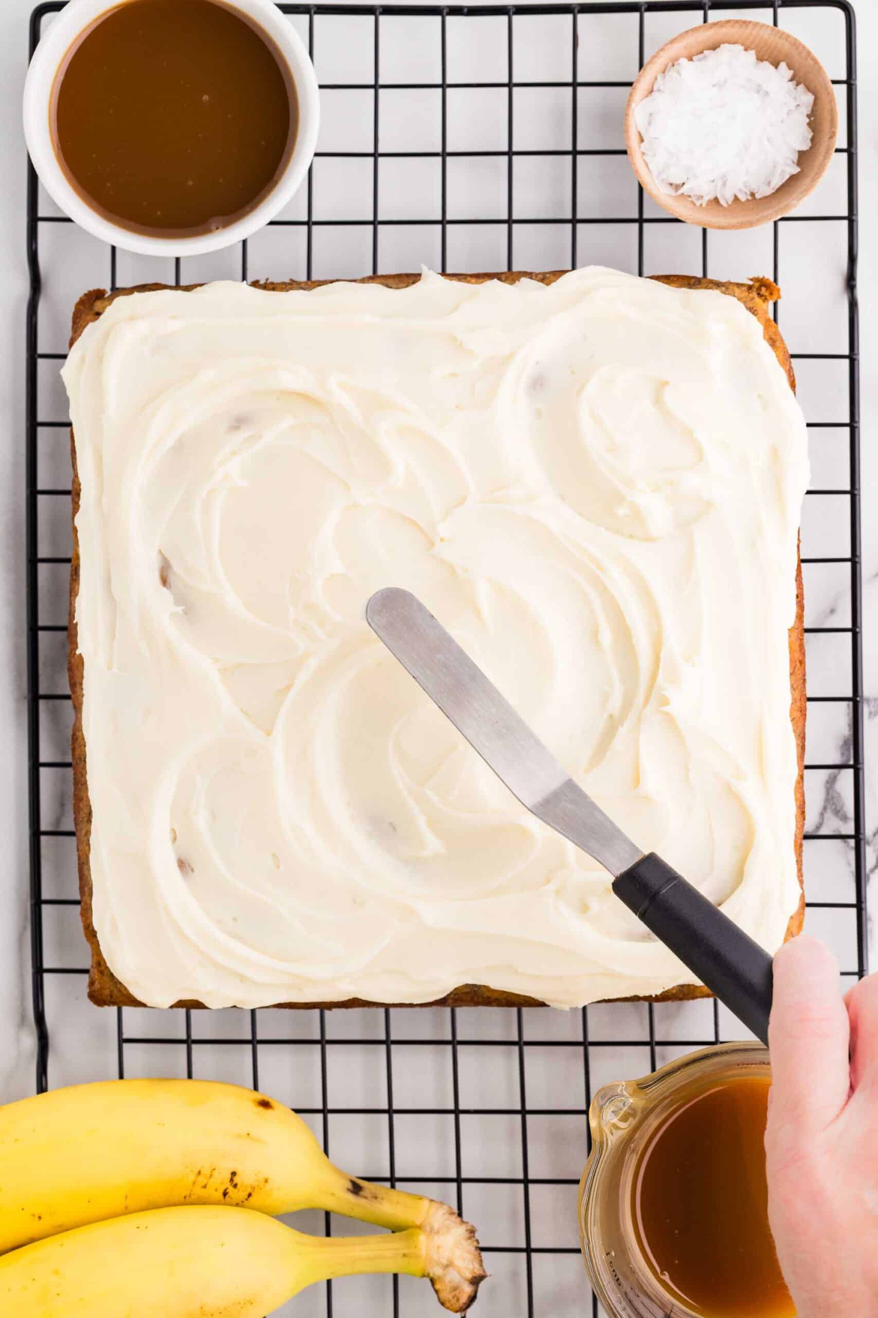 Spreading cream cheese frosting over the banana cake with an offset spatula