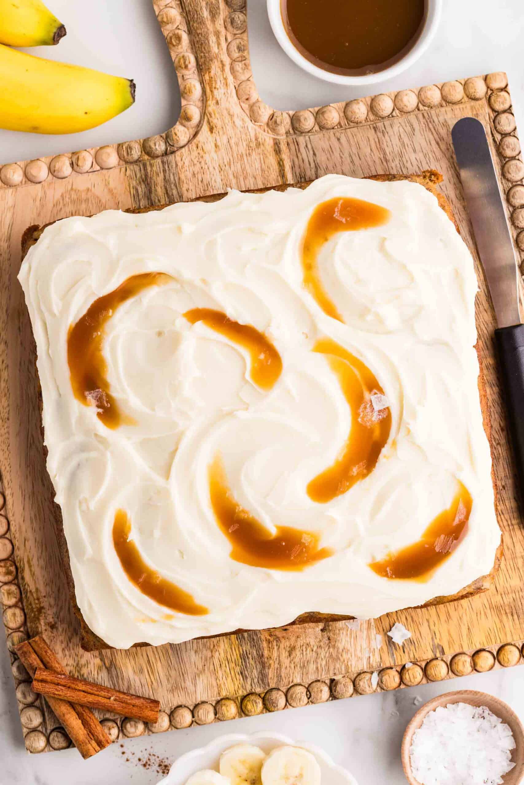 Frosted banana cake swirled with caramel on a wooden board