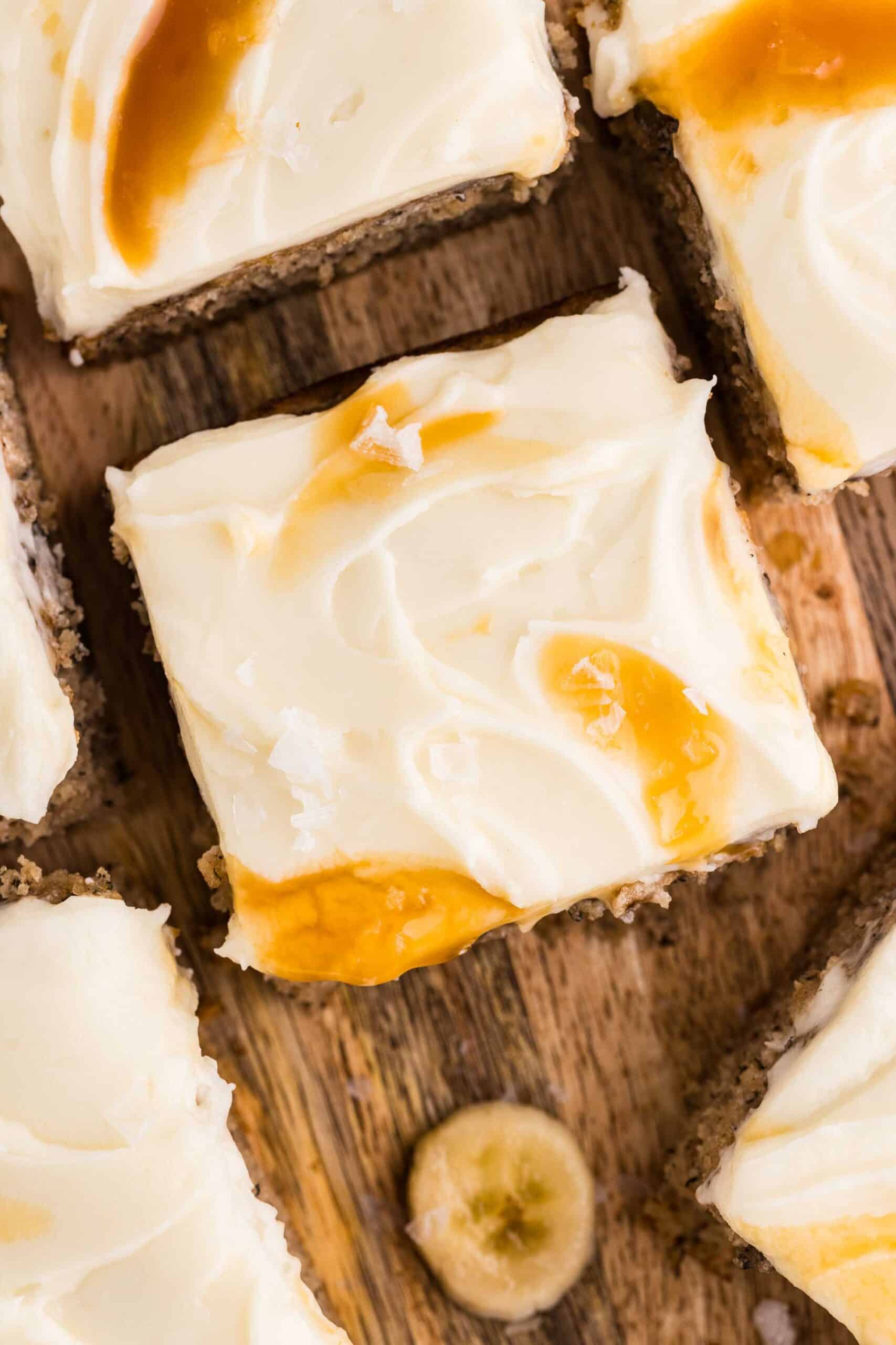 Squares of frosted gluten-free banana cake with caramel swirls on a wooden board