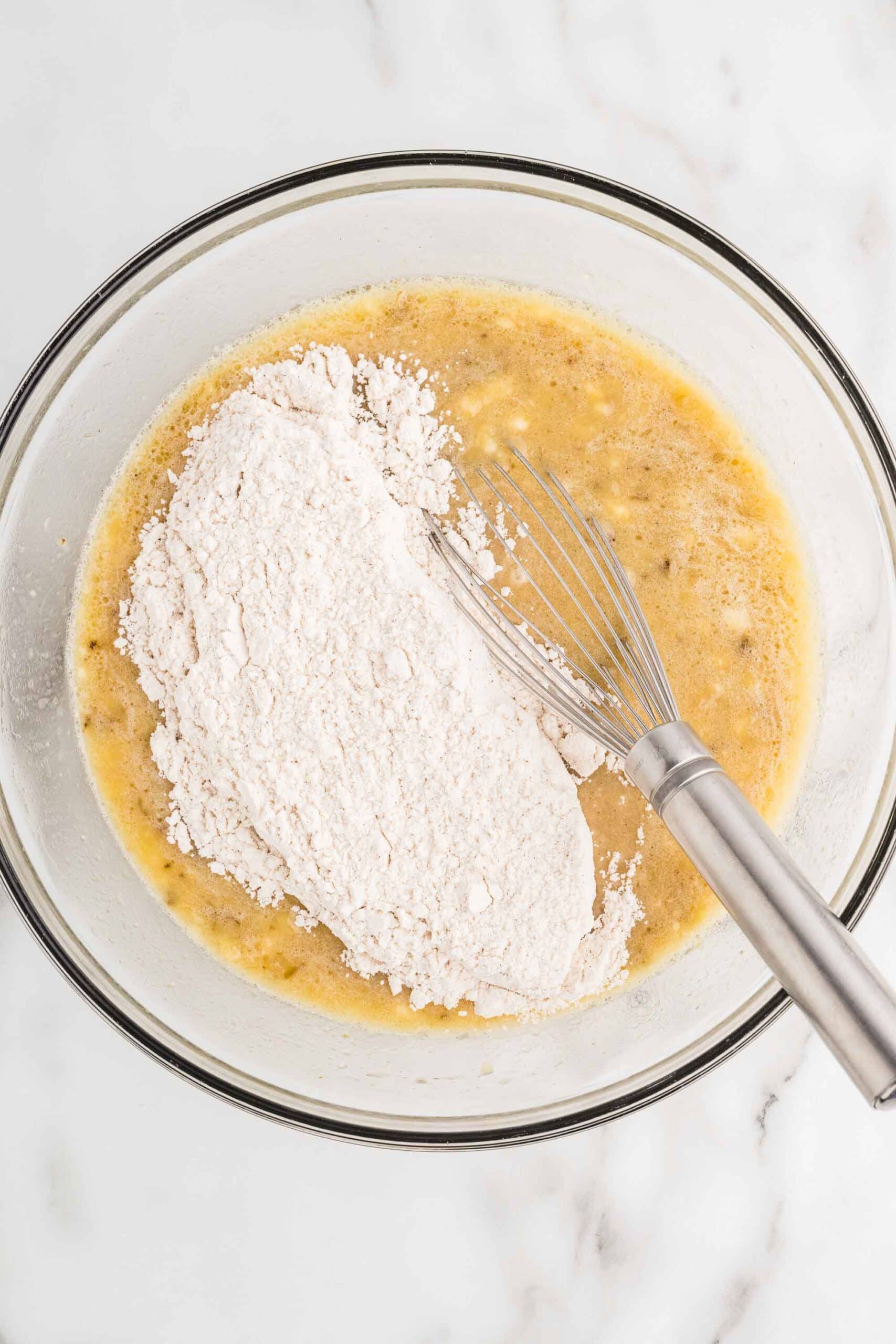 Adding the dry flour mixture to the banana mixture in a glass bowl