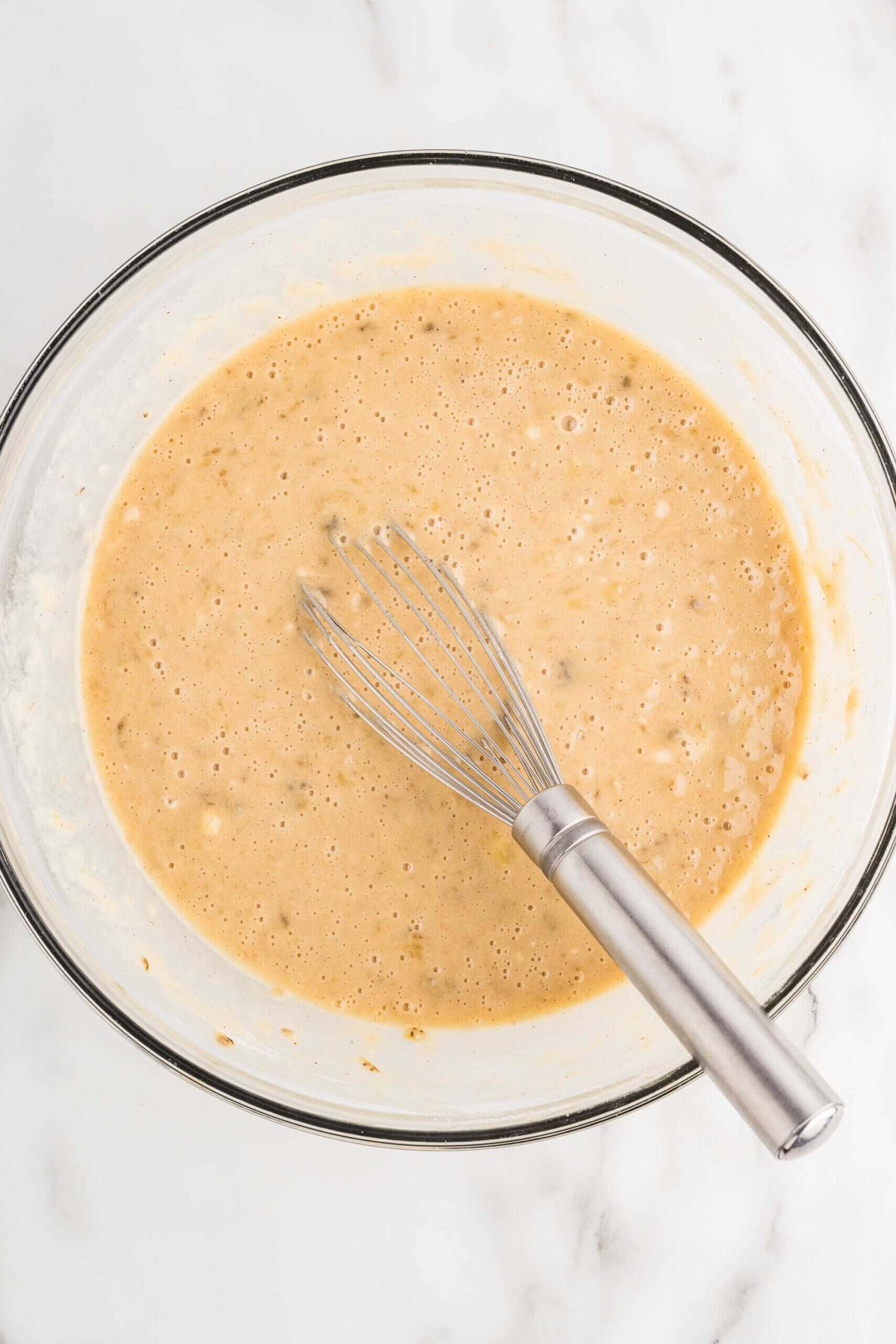 Smooth gluten-free banana cake batter in a glass bowl with a whisk