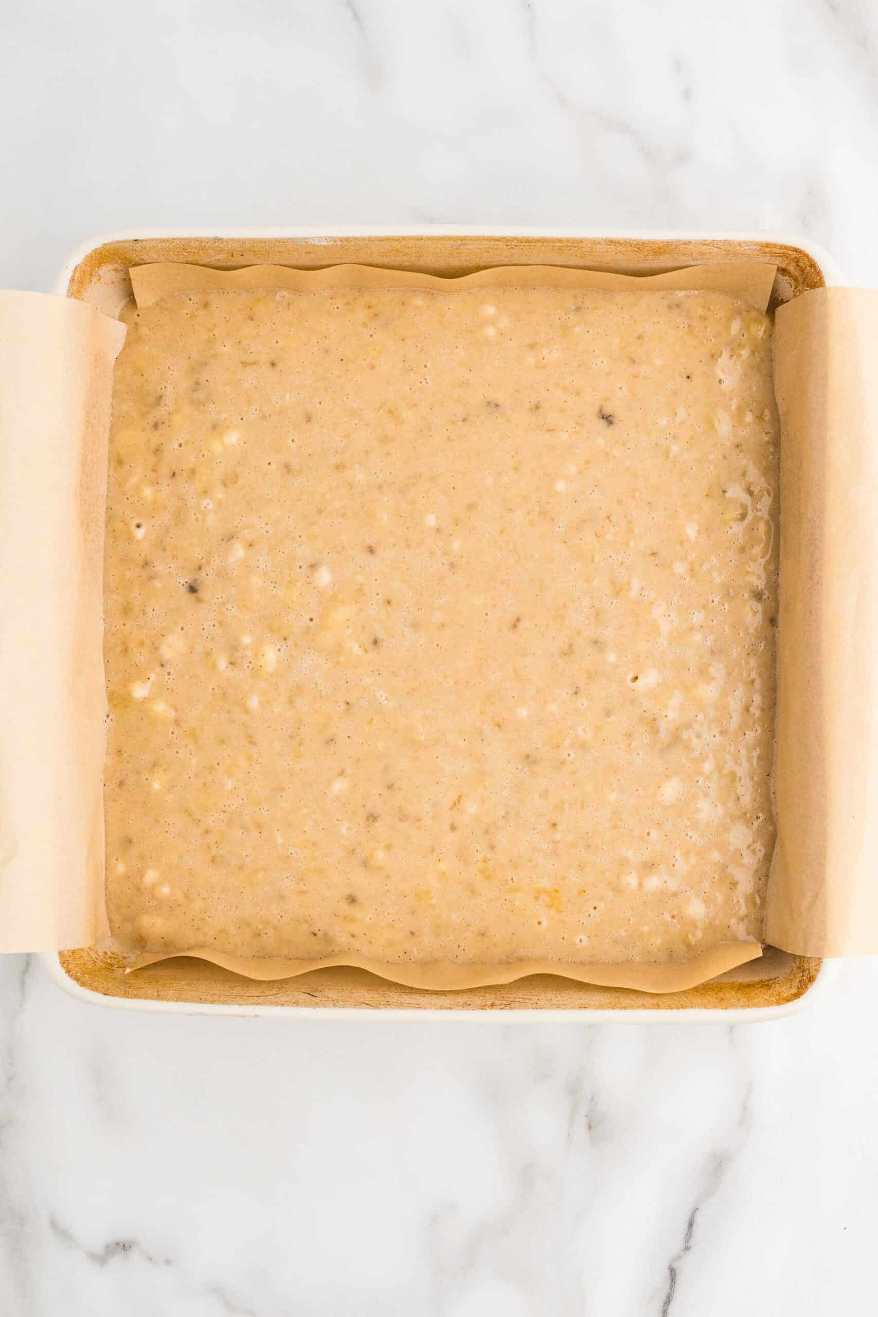 Banana cake batter spread in a parchment-lined square baking pan