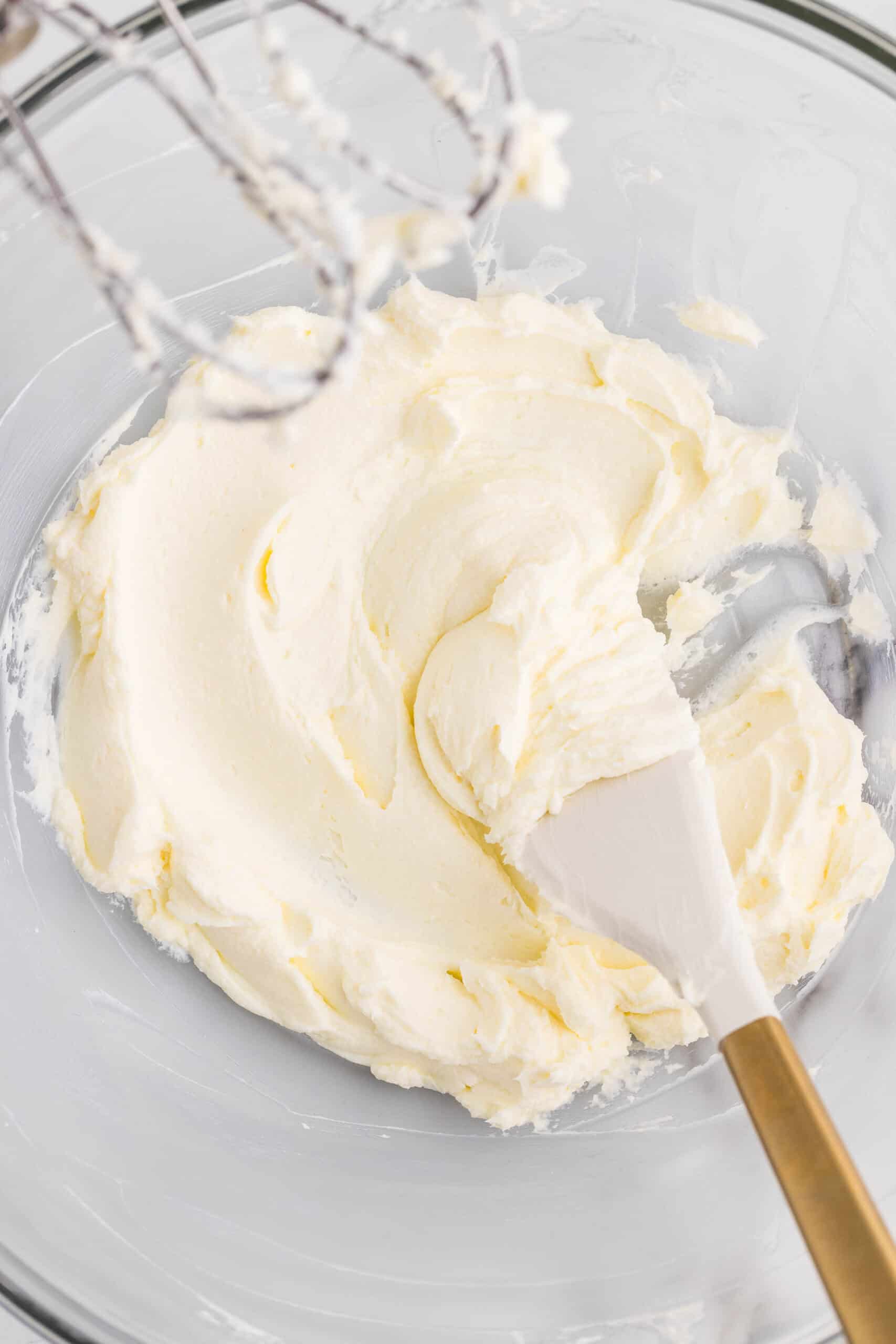 Fluffy maple cream cheese frosting in a glass bowl with a spatula