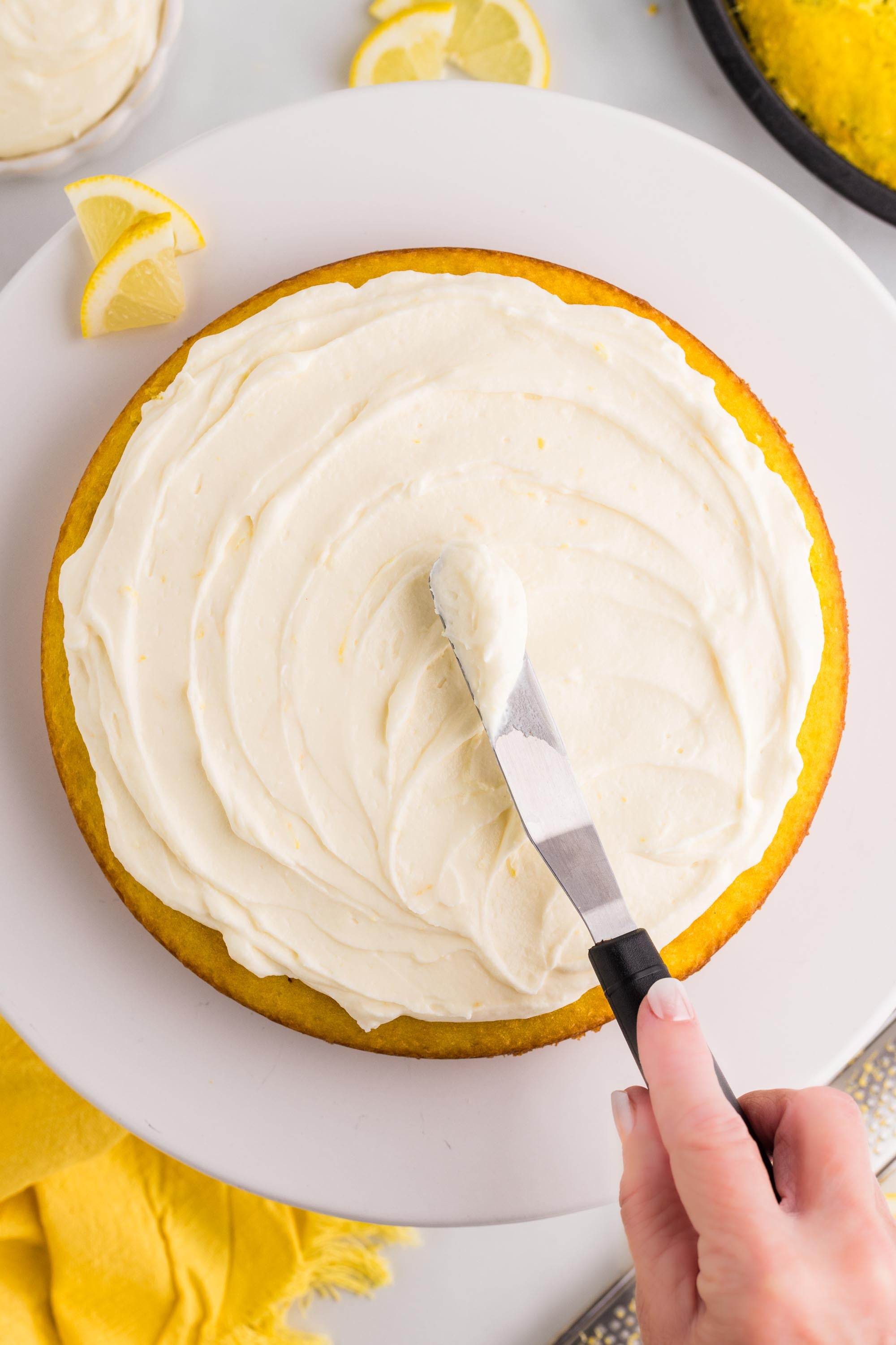 Spreading lemon cheesecake filling over a round lemon cake with an offset spatula