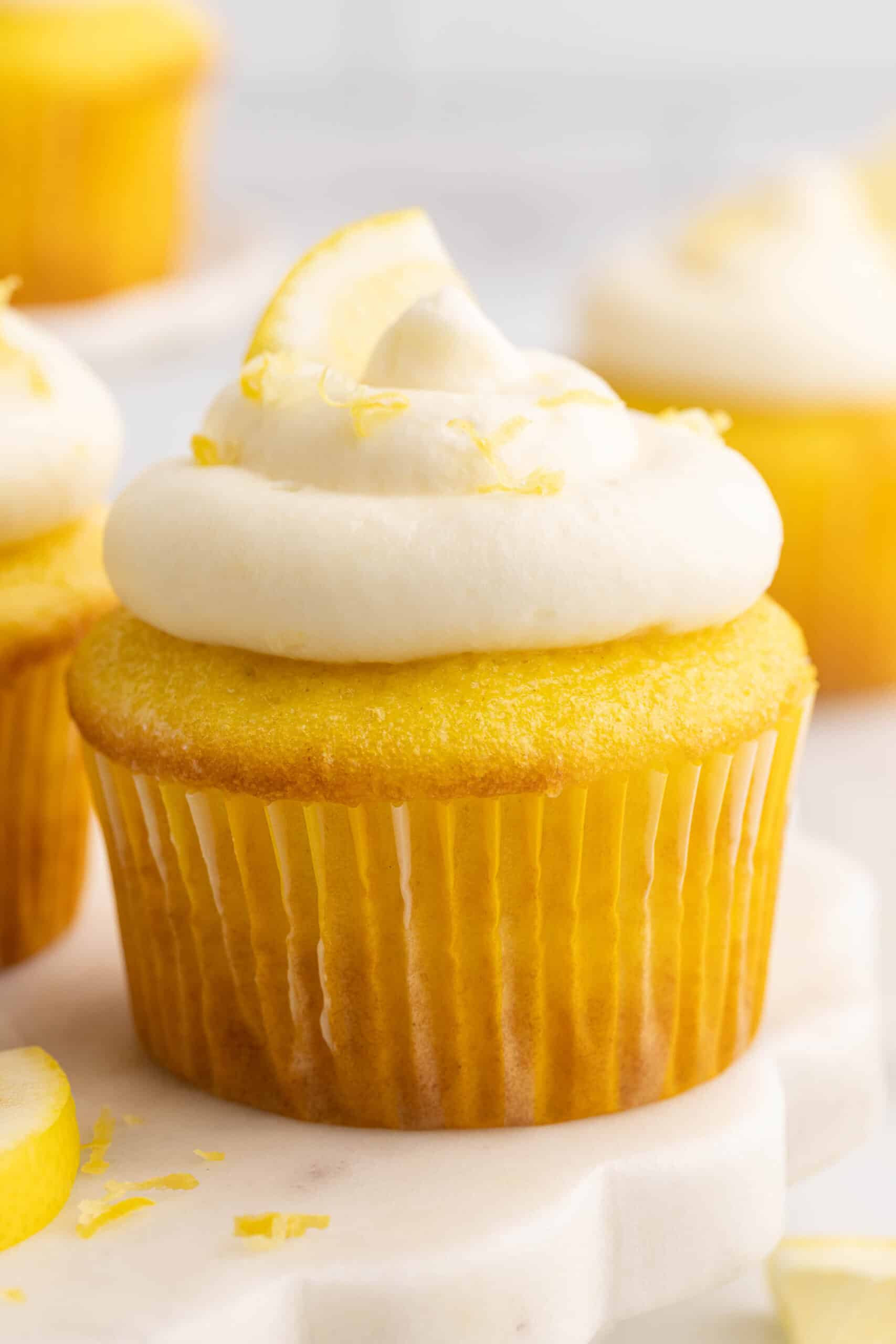 A lemon cupcake topped with a swirl of lemon cheesecake frosting, lemon zest, and a lemon slice