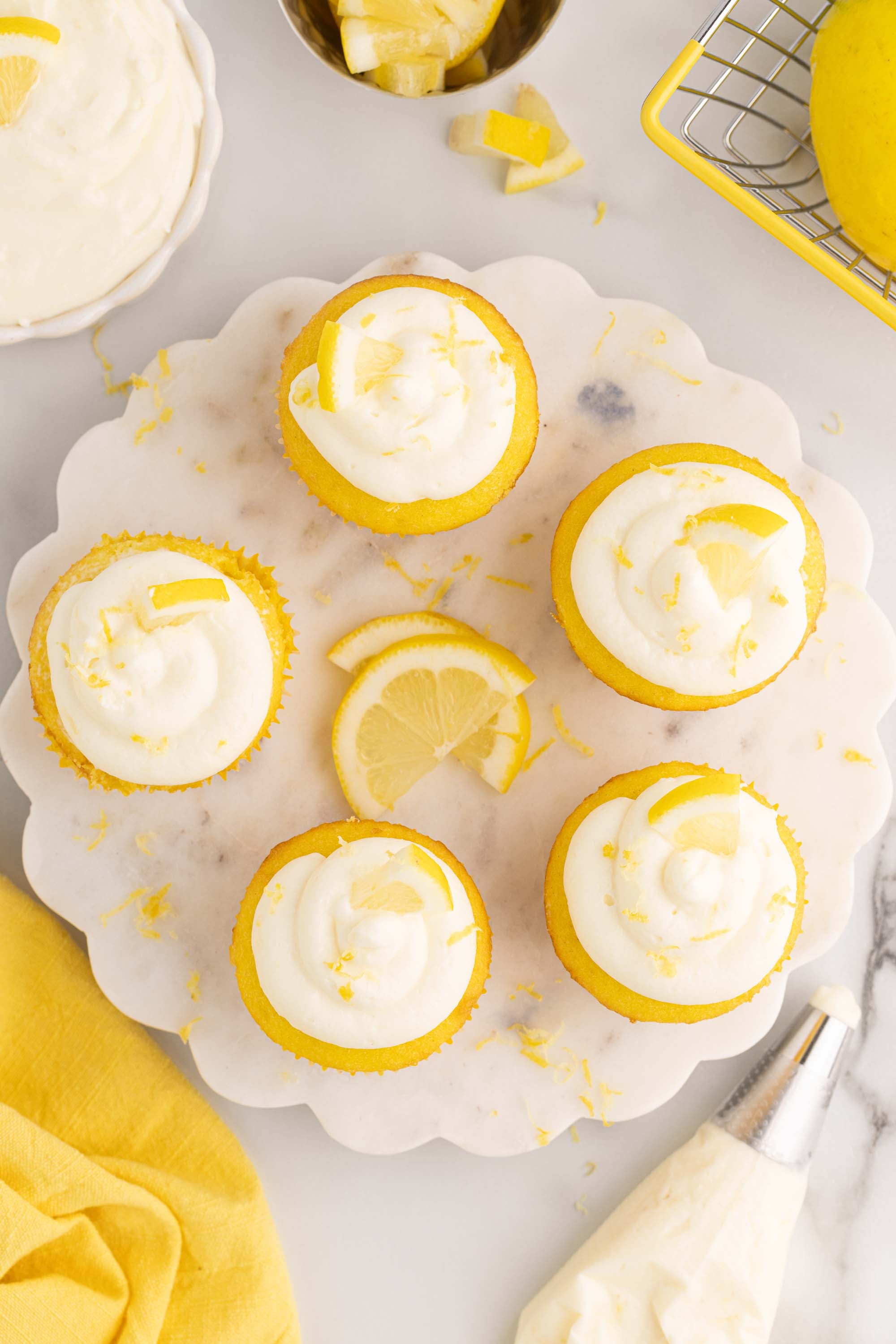 Overhead view of lemon cupcakes piped with lemon cheesecake frosting next to a piping bag